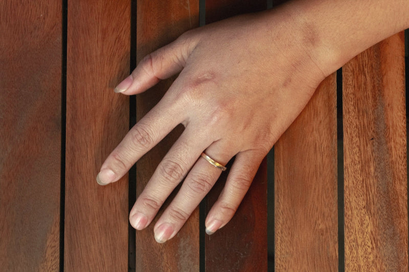 A hand with a single ring resting on a warm wooden table