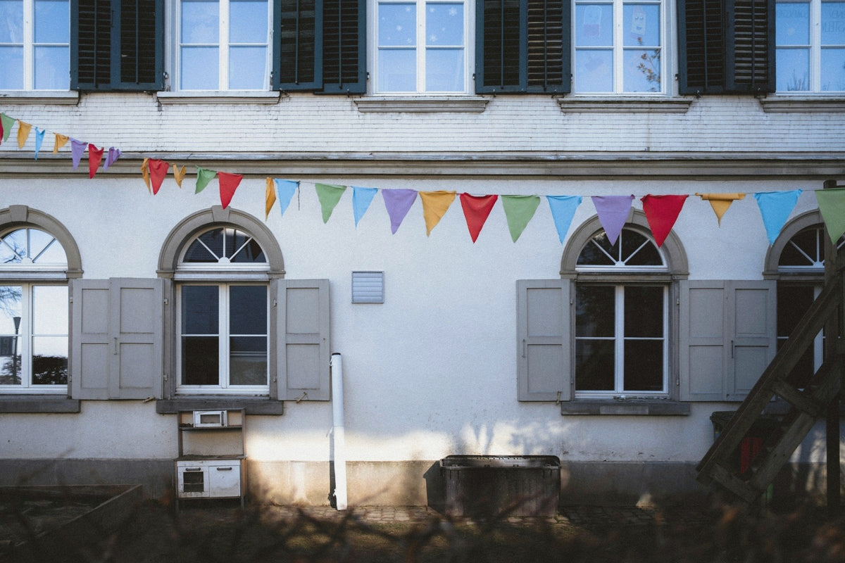 Colored pennant bunting strung across a white building with arched windows and grey shutters