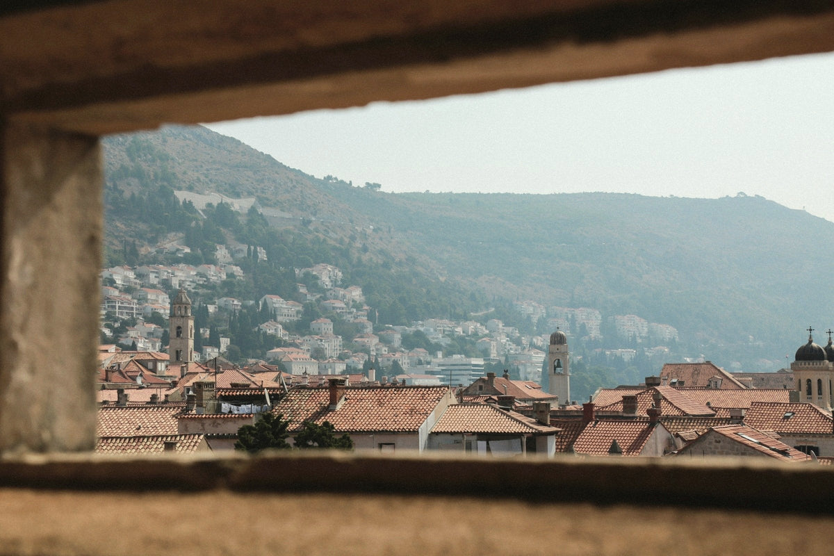 Terracotta rooftops and a green hillside in Dubrovnik, seen through a stone window