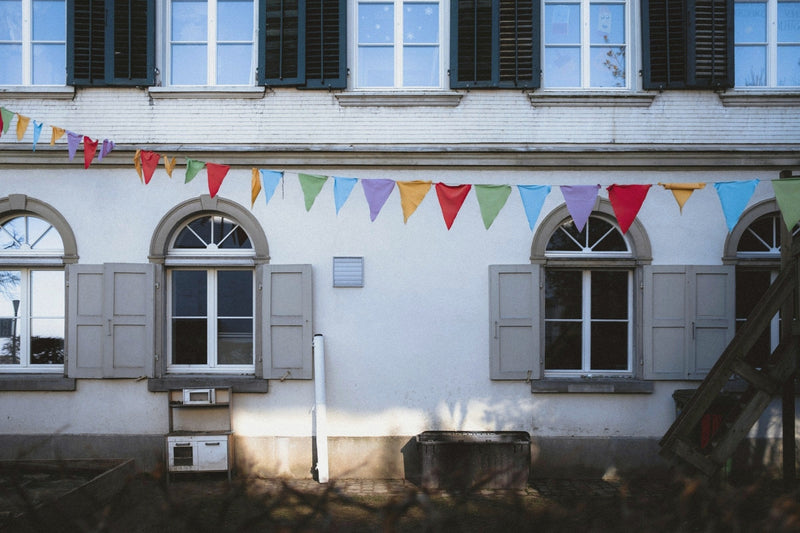 Colored pennant bunting strung across a white building with arched windows and grey shutters