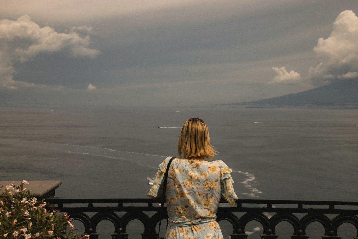 A woman at a balcony rail looking across the Bay of Naples to the far shore