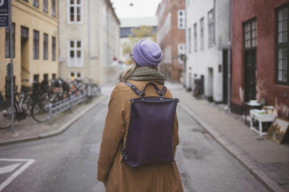 A woman with a leather backpack walking down a quiet old town street, seen from behind