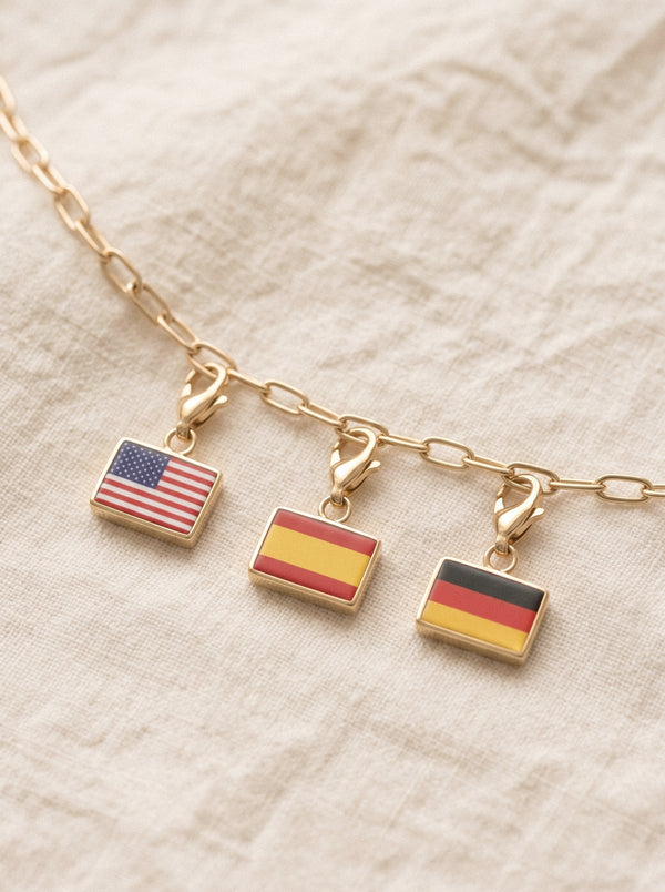 Close up of three flag charms, each on a jump ring and lobster claw, hanging from a gold cable chain on linen